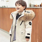 Boys winter coat with hood worn by a smiling boy, cream coat with fluffy hood trim, zip front and snap-flap chest pocket