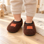 Toddler wearing brown Lumiwee Burrow non-slip slipper socks on a wood floor