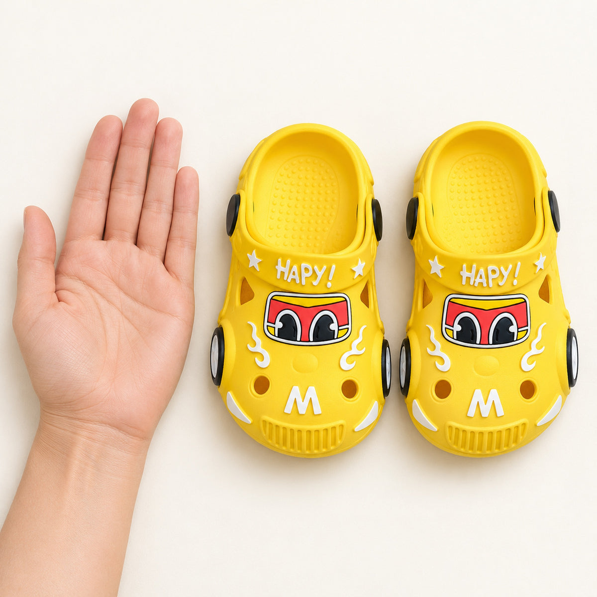 Yellow Lumiwee toddler car clogs beside an adult hand for scale