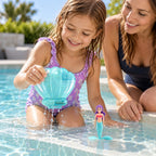 Child retrieving a clear-blue Lumiwee seashell dive toy from a shallow pool with an adult beside her