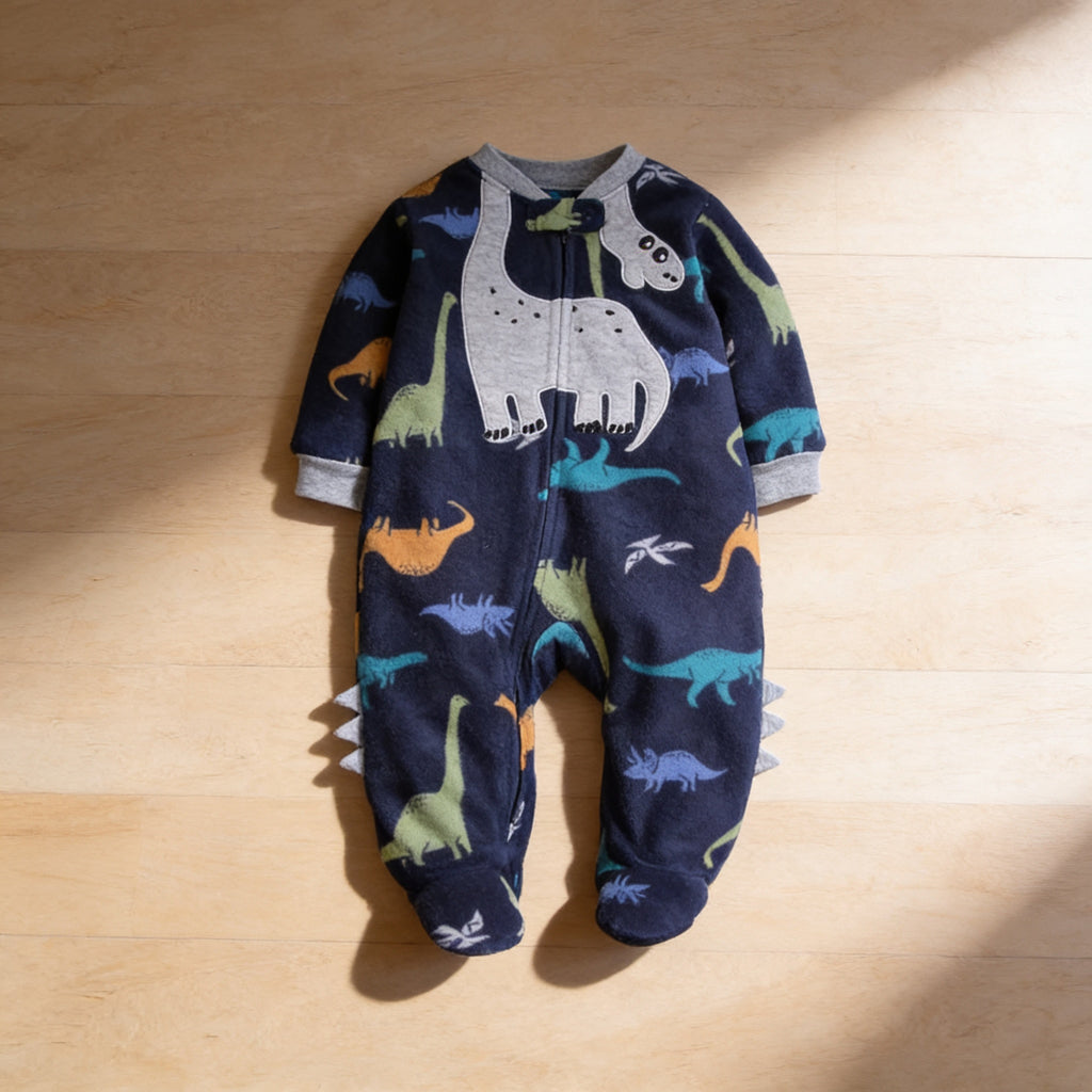 Lumiwee Critter fleece baby romper: the navy dinosaur romper laid flat on a wood floor
