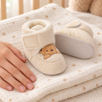 Pair of Lumiwee Brown Bear baby booties beside an adult hand for scale
