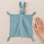 Single blue bunny muslin lovey beside an adult hand for scale