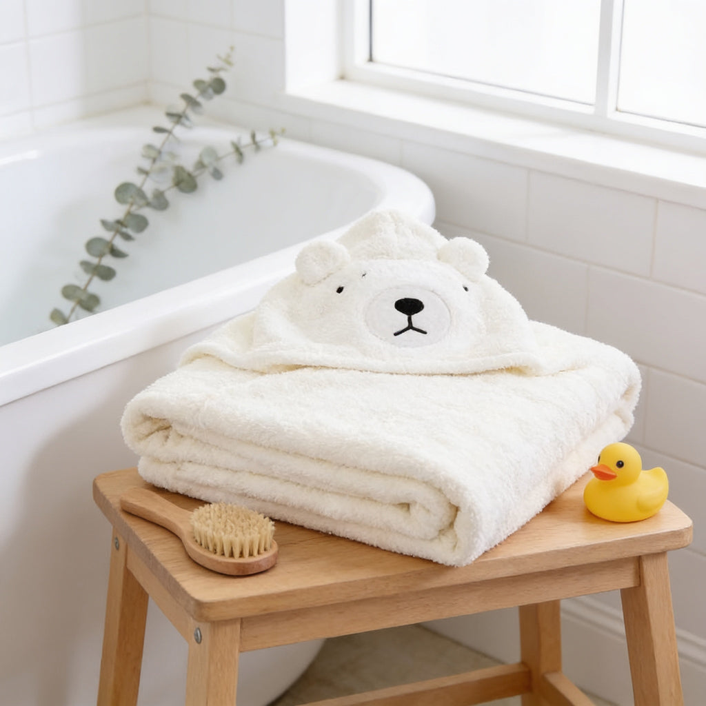 Lumiwee Puddle hooded baby bath towel: cream polar bear hooded towel folded on a bathroom stool