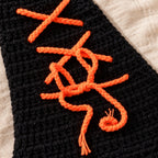 Close-up of orange yarn lacing and bow on the black crochet cloak