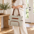 Adult carrying the Khaki pinstriped diaper tote by both handles in a home entryway